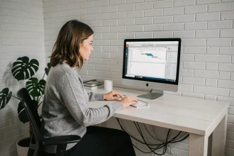 Femme travaillant sur un ordinateur fixe dans un bureau à domicile minimaliste avec une grande plante verte et un bureau en chêne blanc